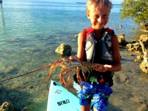 A boy holds a lobster on a Solo Skiff